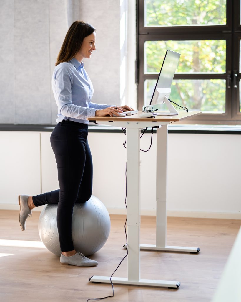 Woman Using Adjustable Height Standing Desk In Office For Good Posture