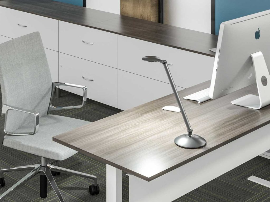 The image shows a task light on top of a work station. A chair, cabinets, and computer can also be seen in the image.